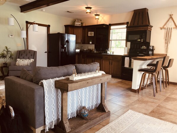 A cozy living room with a sofa, a wooden coffee table, and a kitchen area with dark wooden cabinets and a black refrigerator.