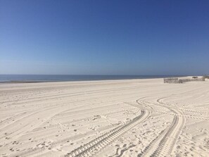 A sandy beach with tire tracks leading to a structure in the distance.