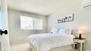 A bedroom with a bed, a nightstand, a window, and a wall-mounted air conditioner.