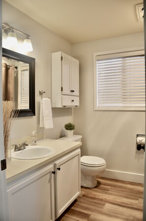 A bathroom with a white sink, mirror, and cabinet, a toilet, and a window with blinds. - Adorable Farm Stay in Ballard! Bunnies, A/C, walkable, near beach & attractions (Seattle)