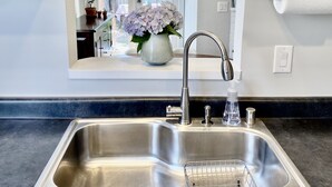 A modern kitchen with a stainless steel sink, a faucet, and a soap dispenser. There is a potted plant with purple flowers on the counter.