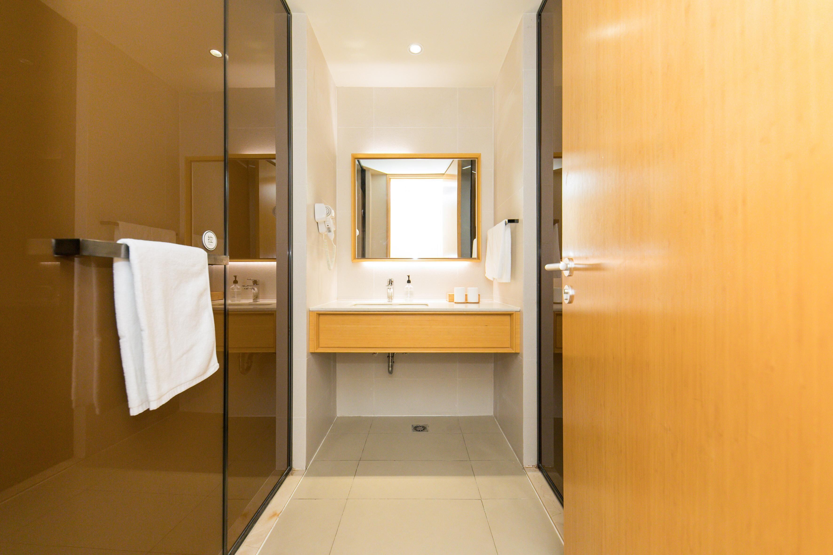 A modern bathroom with a glass shower enclosure, a wooden vanity, and a large mirror.