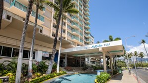 Um hotel com piscina, palmeiras e uma placa com a inscrição 'Aqua-Aloha Surf'.