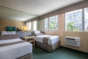 Hotellihuone, jossa on kaksi sänkyä, pieni pöytä, lamppu ja suuri ikkuna, josta avautuu näkymä korkeaan kerrostaloon ja vehreään maisemaan.