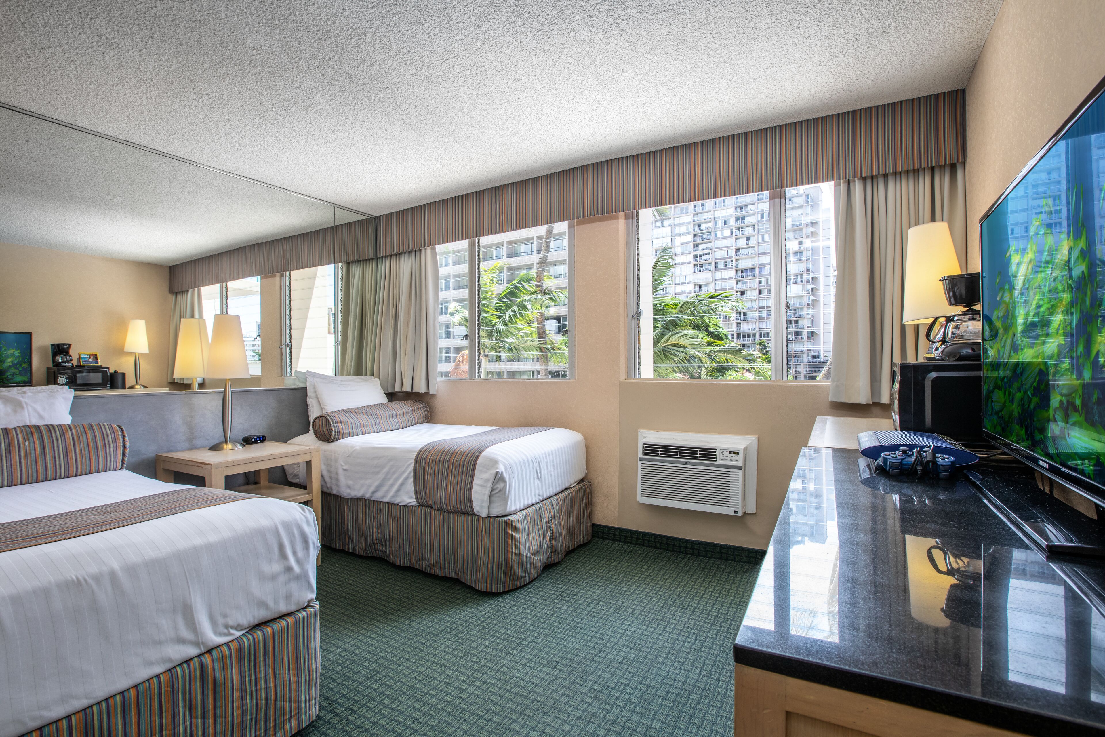 A hotel room with two beds, a desk with a TV, and large windows with curtains.