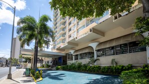 A modern hotel with a pool, outdoor seating, and a sign listing amenities like fresh juice and cocktails. - Aqua Aloha Surf Waikiki 313 | Downtown City Views – Pool & BBQ (Honolulu)