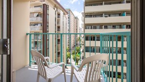 A balcony with two white plastic chairs, a turquoise railing, and a view of multi-story buildings in the background.