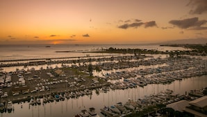 A marina with numerous boats docked, a parking area with cars, and a view of the sunset over the water.