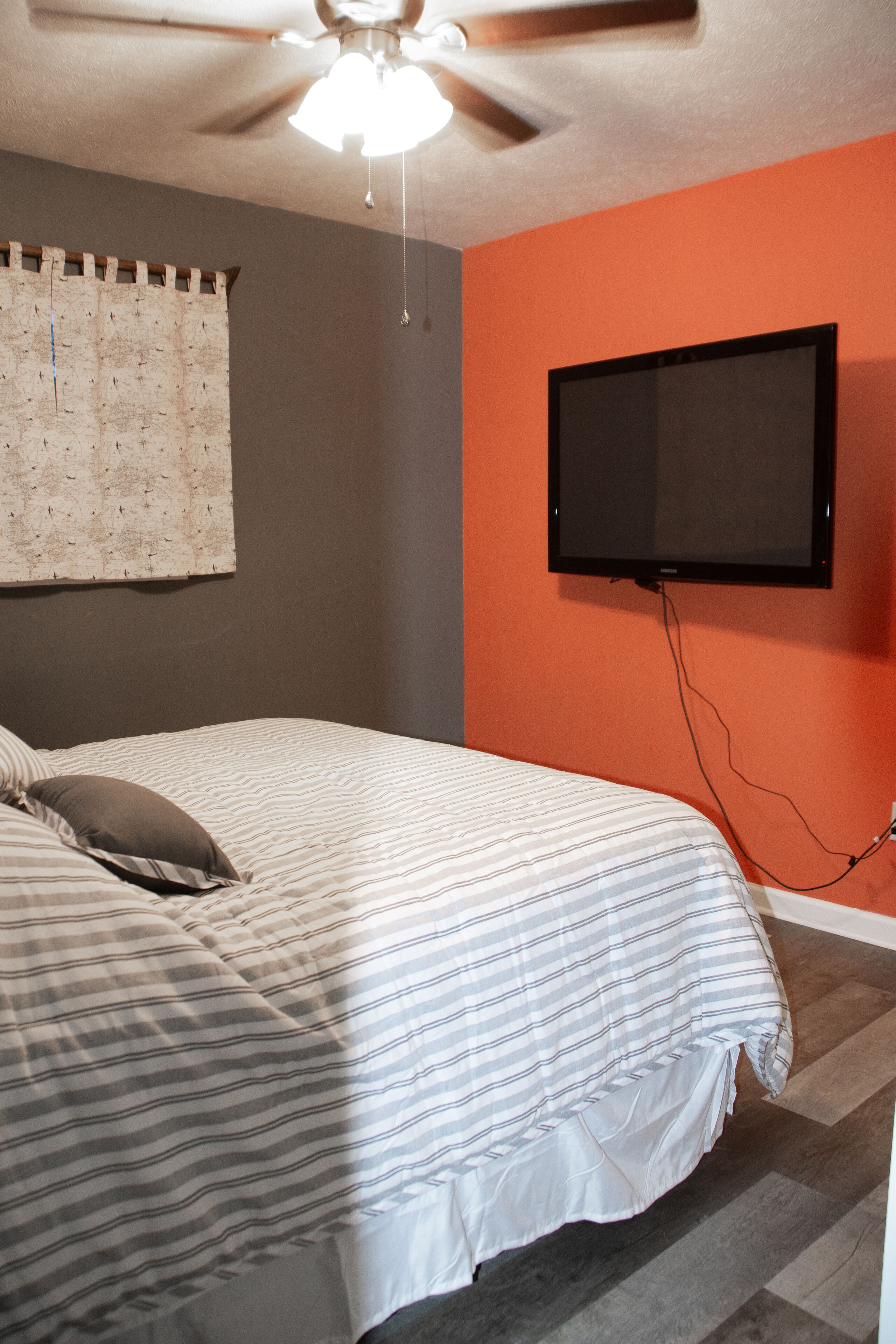 A bedroom with a bed, a ceiling fan, a wall-mounted TV, and a window with curtains.