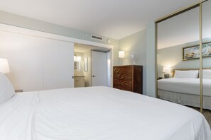 Une chambre d’hôtel avec un grand lit, une armoire en bois, un miroir et une porte donnant sur une autre pièce.