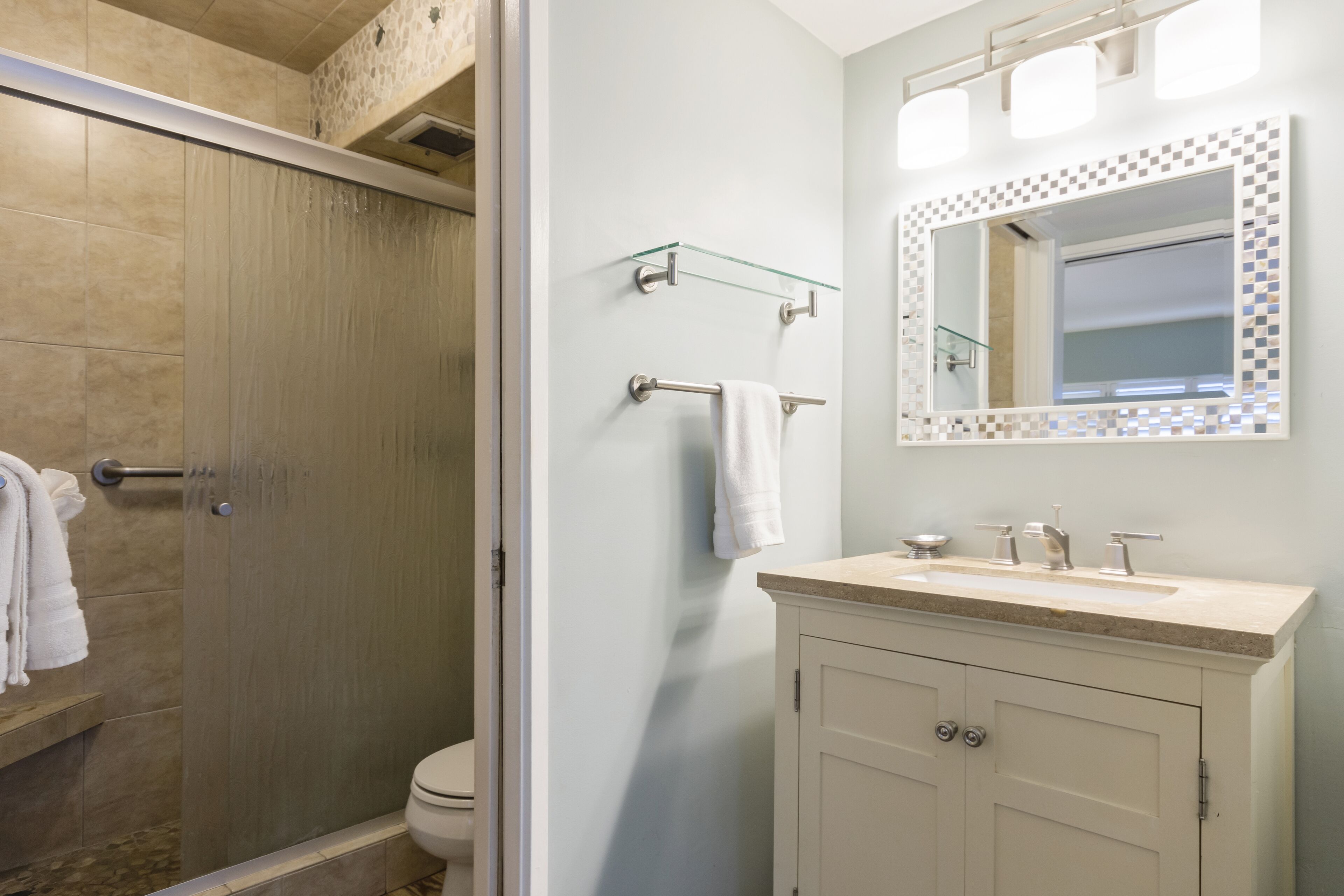 A bathroom with a shower, toilet, vanity with a sink, and a mirror with a decorative frame.
