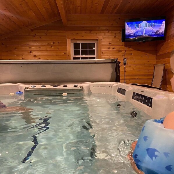 L’intérieur d’un chalet en bois, avec un jacuzzi, un téléviseur fixé au mur et une fenêtre.