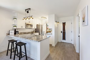 Eine moderne Küche mit weißen Schränken, Granit Arbeitsplatten und einer zentralen Kochinsel mit Barhocker.