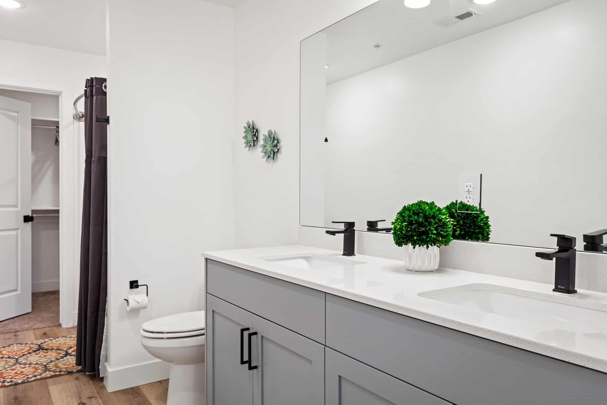 Un baño moderno con un lavamanos blanco, grifo negro y un espejo grande. Se ve un inodoro y una cortina de ducha.
