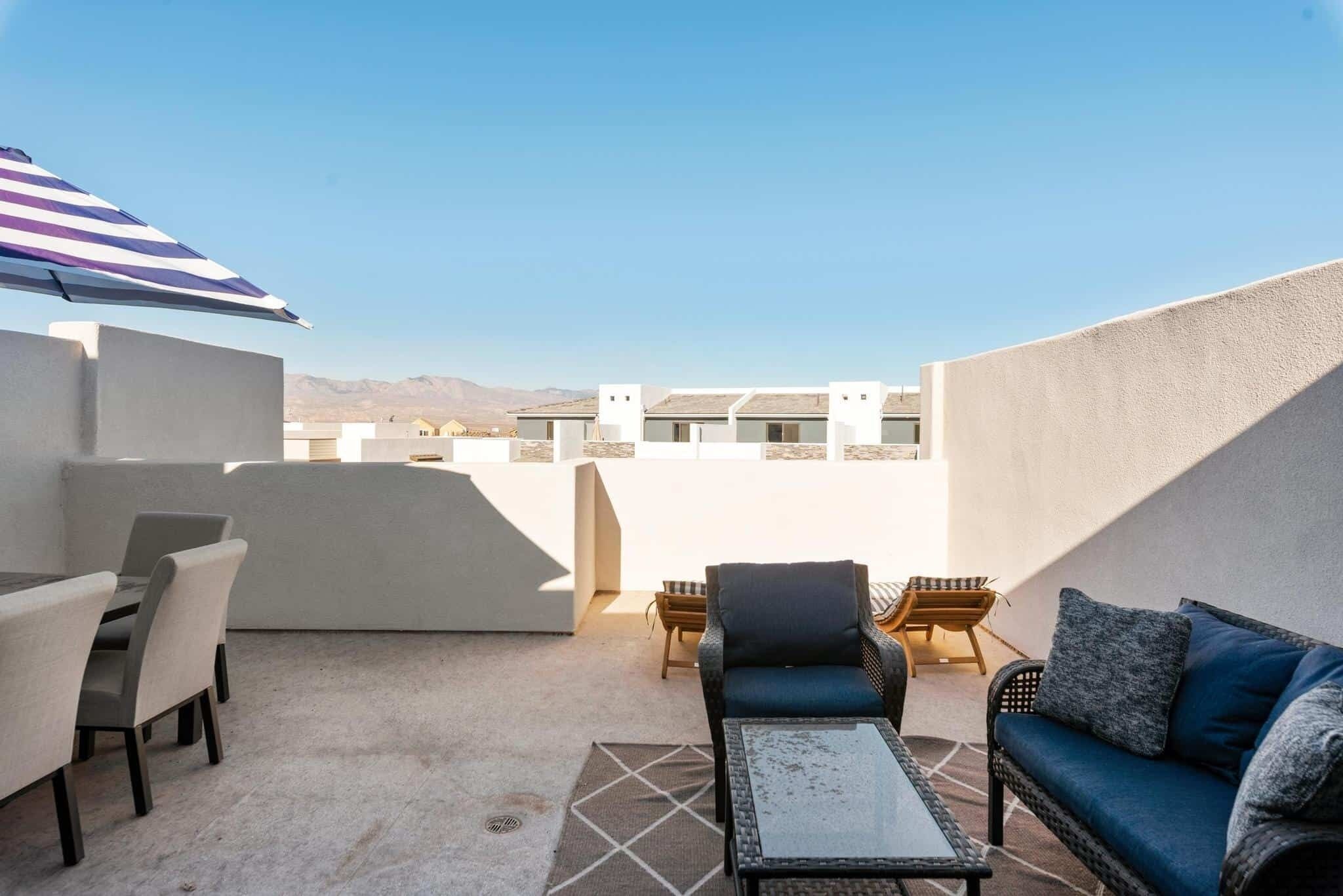 A rooftop terrace with a dining table, chairs, a sofa, and an umbrella.
