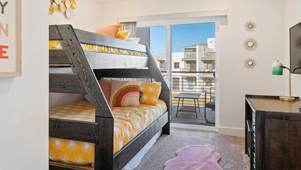 A bedroom with a bunk bed, a desk, and a balcony with a view of buildings.