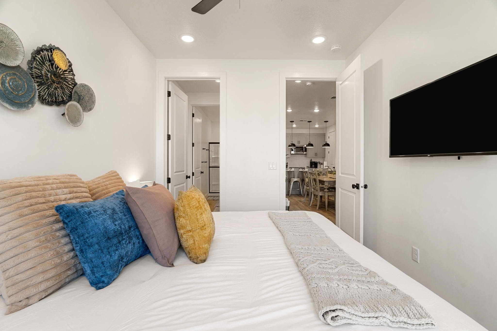 Ein Schlafzimmer mit einem Bett, Kissen, einem Fernseher und einer Küche im Hintergrund.