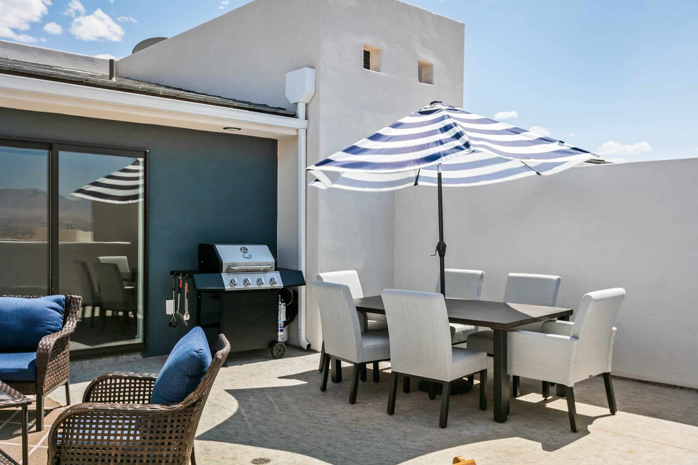 An outdoor patio with a grill, dining table, chairs, and a striped umbrella.