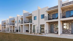 A row of modern multi-story residential buildings with balconies, large windows, and a well-maintained lawn in front.