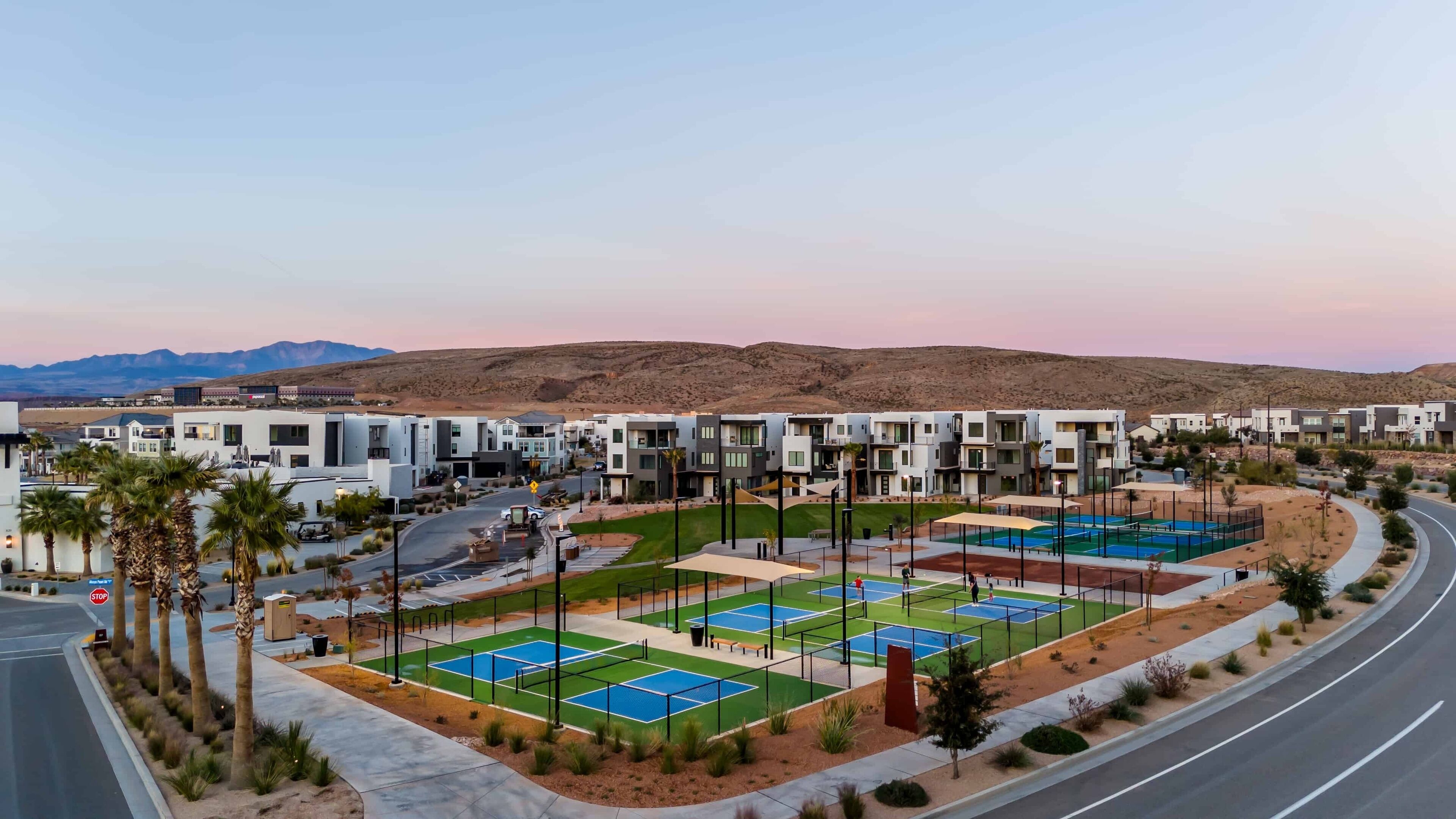 A modern residential area with multiple-story houses, a tennis court, and a road curving around the property.
