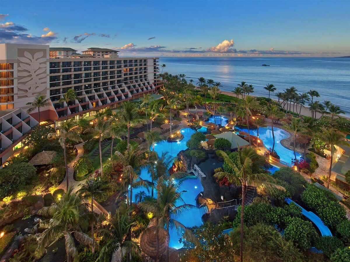 A resort with multiple swimming pools surrounded by palm trees and a large hotel building.