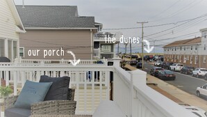 A balcony with wicker furniture and a white railing overlooking a street with parked cars and buildings. - Newly Furnished Open Air Home, Steps to the Beach (Seaside Park)