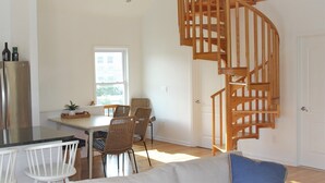 A modern kitchen with a built-in refrigerator, a dining area with wicker chairs, and a wooden spiral staircase leading to an upper level. - Newly Furnished Open Air Home, Steps to the Beach (Seaside Park)