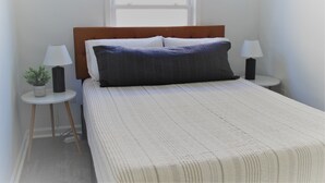 A neatly made bed with a striped bedspread, two bedside lamps, a small potted plant, and a window in the background. - Newly Furnished Open Air Home, Steps to the Beach (Seaside Park)
