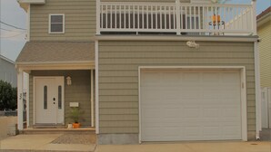 A two-story house with a front garage door, a small balcony with a railing, and a single window on the upper floor. - Newly Furnished Open Air Home, Steps to the Beach (Seaside Park)