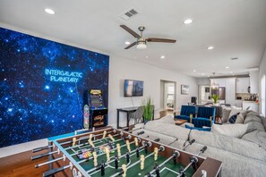 Uma sala de estar com mesa de futebol, um sofá e uma parede com um mural com tema espacial.