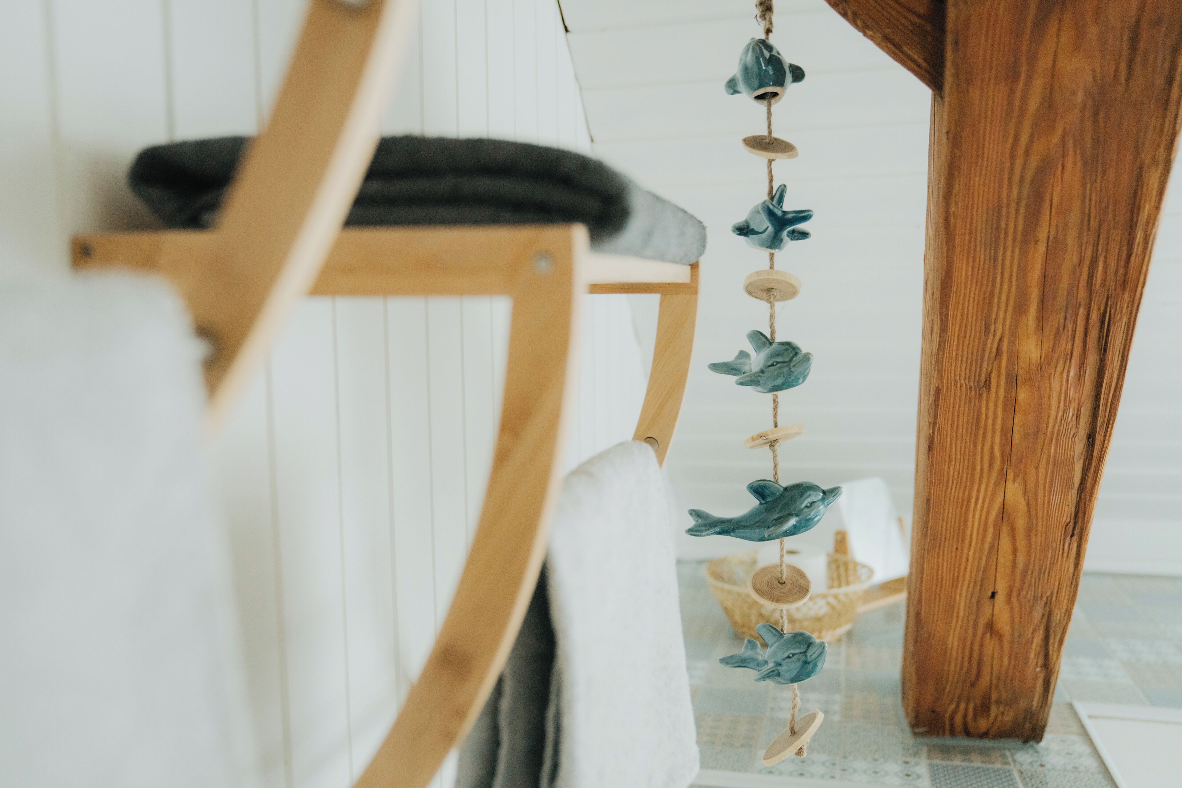 A wooden chair with a white cushion, a hanging mobile with blue and green elements, and a wooden floor.