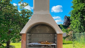 Un horno de pizza de piedra al aire libre con chimenea, rodeado de césped y árboles.