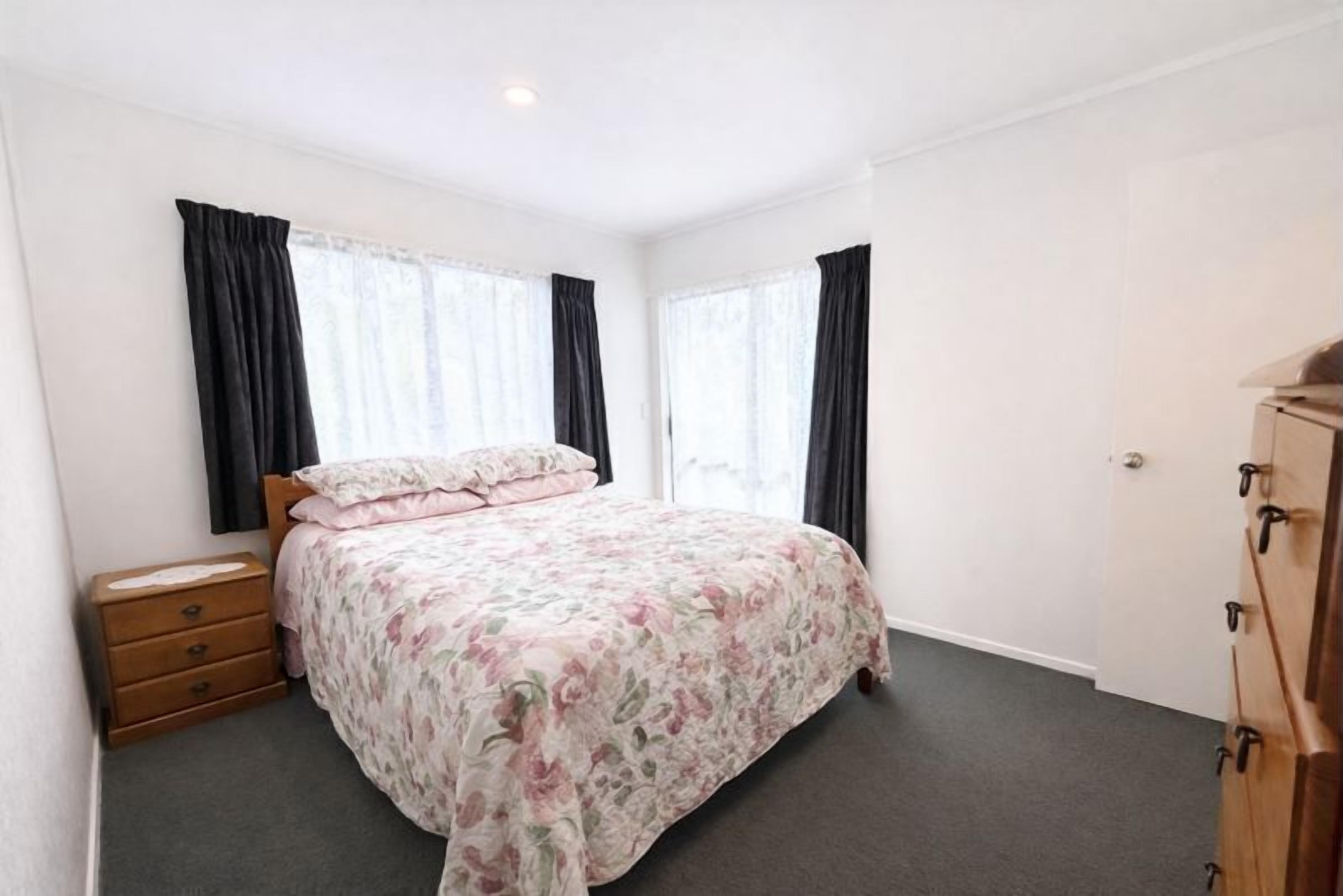 Um quarto com uma cama, uma cômoda de madeira e uma janela com cortinas.