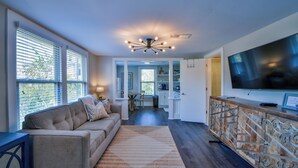 A modern living room with a sofa, a TV, and a decorative cabinet. - Oak - Walk to the Stadium!  Backyard with firepit & grill (Tuscaloosa)