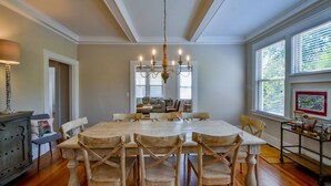 A dining room with a large wooden table and chairs, a chandelier, and a view of the kitchen through a doorway. - Oak - Walk to the Stadium!  Backyard with firepit & grill (Tuscaloosa)