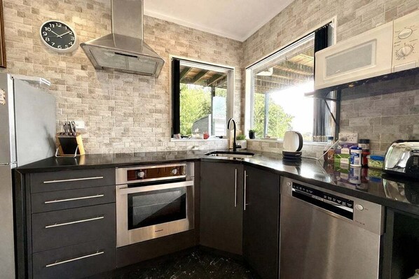 A modern kitchen with a brick backsplash, stainless steel appliances, and a window providing natural light.