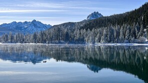 A tranquil lake with snow-covered trees and mountains in the background.