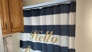 Un baño con cortina de ducha a rayas que muestra la frase 'Hello Beautiful' en letras doradas.
