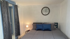Un dormitorio con una cama, una mesita de noche, un reloj de pared y una pieza de arte en la pared con forma de árbol decorativo.