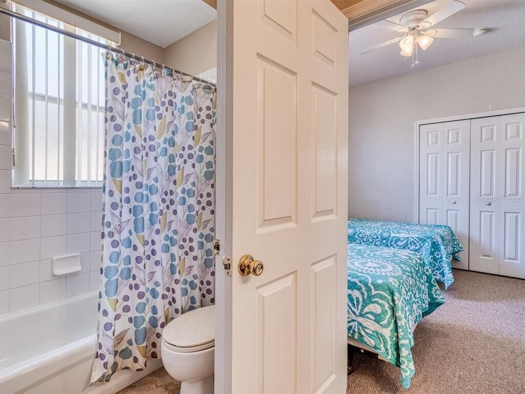 Een badkamer met een toilet, een douchegordijn met een bloemendesign en een bed met een blauw-witte sprei.