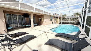 Un espacio al aire libre cubierto con piscina, sillones de descanso y una zona de estar con mesas y sillas.
