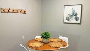 Un comedor con una mesa redonda, cuatro sillas, una pequeña planta en maceta e ilustraciones de plantas enmarcadas en la pared.