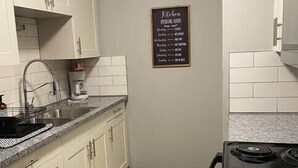 Una cocina compacta con armarios blancos, encimera de granito, estufa negra y piso de madera.