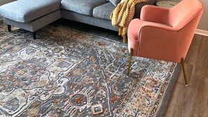 Una sala de estar con un sofá modular gris, un sillón rosa y una alfombra estampada.