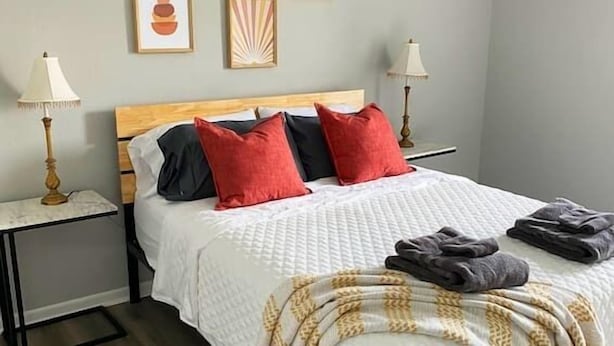 Un dormitorio ordenado con una cama, dos mesitas de noche y cuatro cuadros enmarcados en la pared.