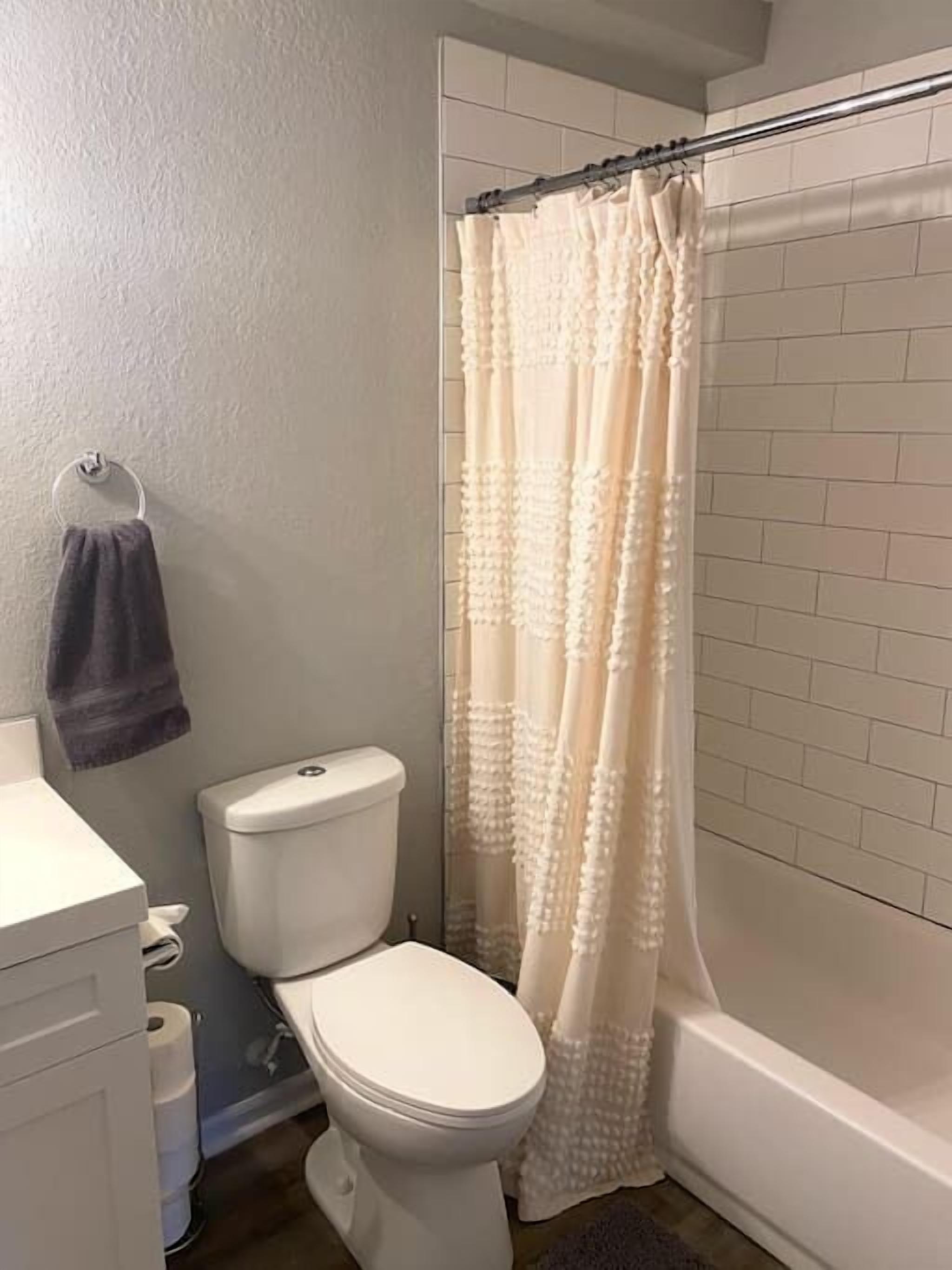 Un baño con inodoro, toallero con toalla y cortina de ducha.