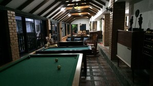 Une table de billard recouverte d’un drap vert, avec une bille blanche, entourée de murs en briques et de poutres en bois.