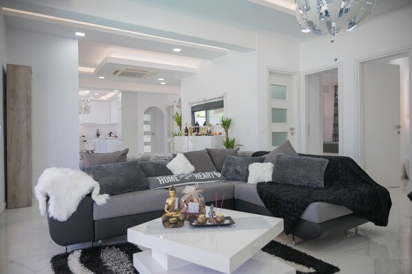 A modern living room with a grey sofa, a white coffee table, and a decorative Buddha statue.