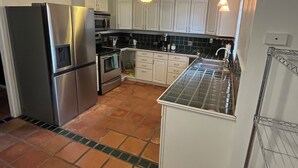 A compact kitchen with white cabinets, stainless steel appliances, and a tiled backsplash. - The Ranger House, 5 minutes to TAMU campus, quiet street, large fenced backyard (Bryan)