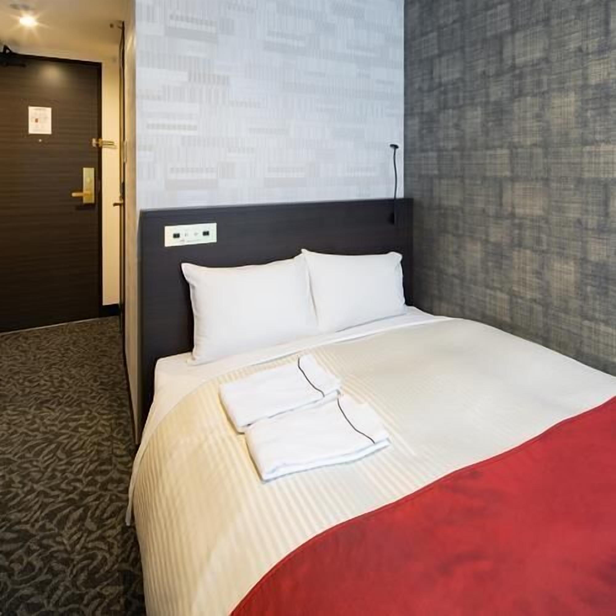 A hotel room with a bed, a headboard, a wall with a patterned design, and a carpeted floor.